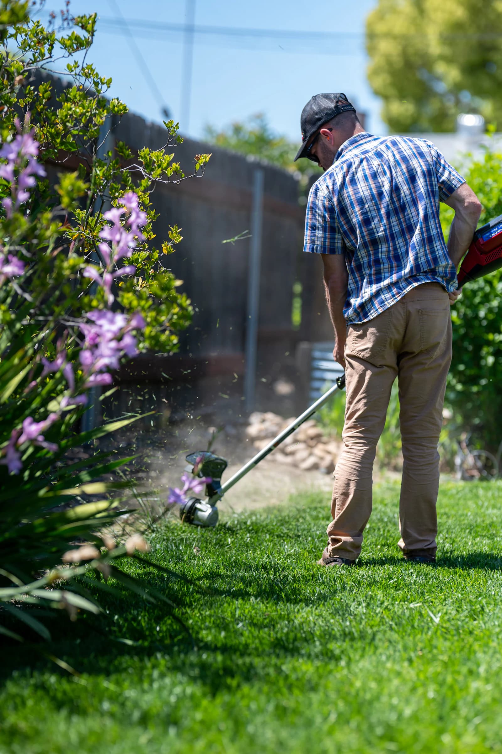 A person using a string trimmer beside a garden